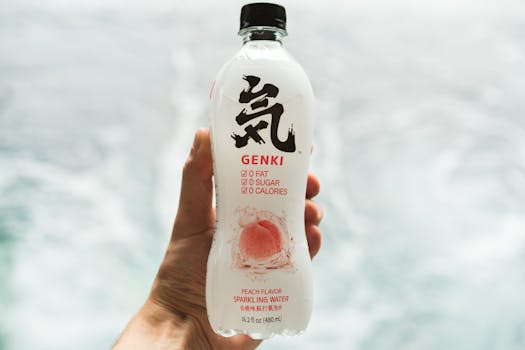 Hand holding a Genki peach-flavored sparkling water bottle against a blurred background.