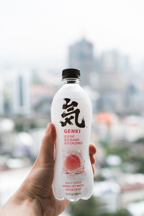 Free Person holding Genki peach sparkling water bottle with city background. Stock Photo
