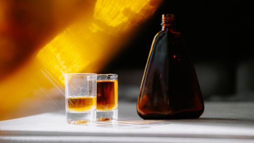 Free A warm sunbeam highlights an amber bottle and glasses, creating a serene still life. Stock Photo