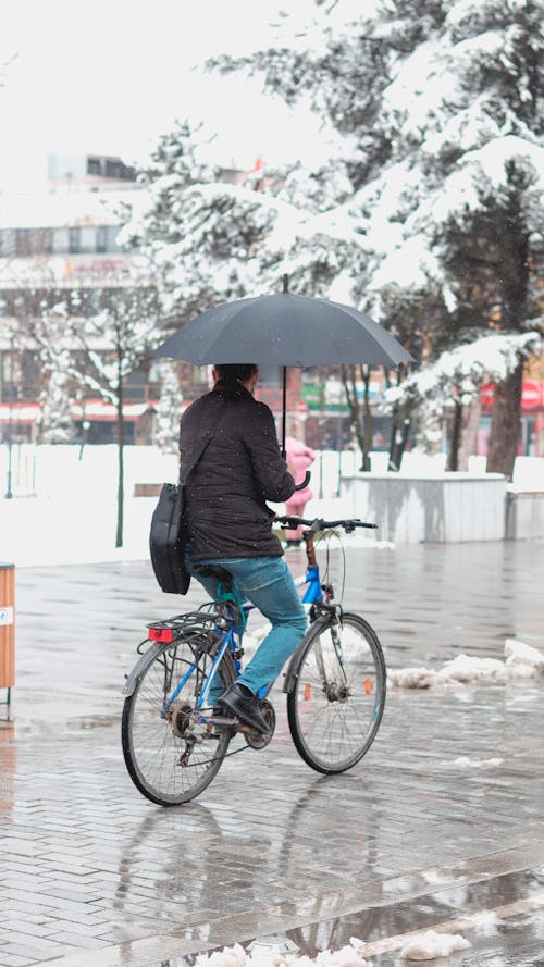 Man in Black Jacket Holding an Umbrella While Riding Bicycle