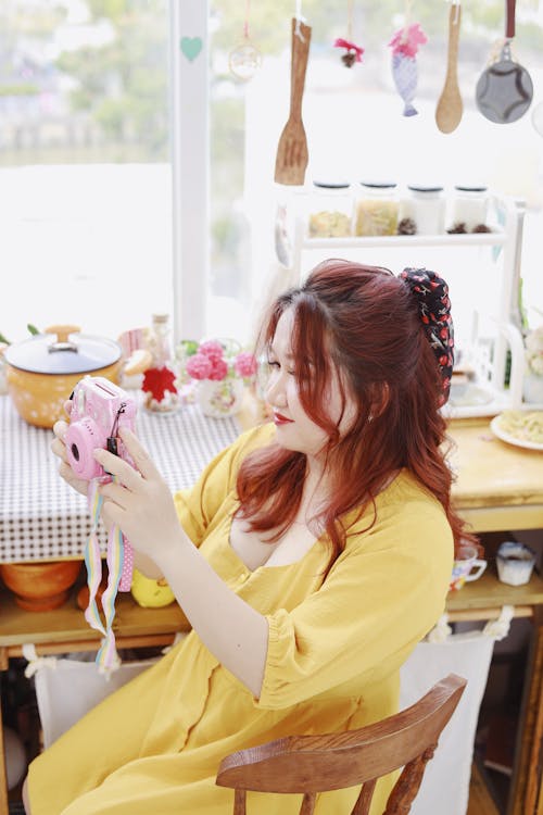 A Woman in a Yellow Dress Taking a Picture with an Instant Camera