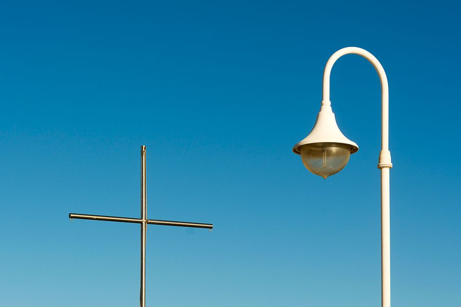 A minimalist view of a cross and lamp post against a clear blue sky.