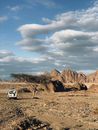 White Van on Dirt Road Near Brown Rock Formation Under White Clouds and Blue Sky during