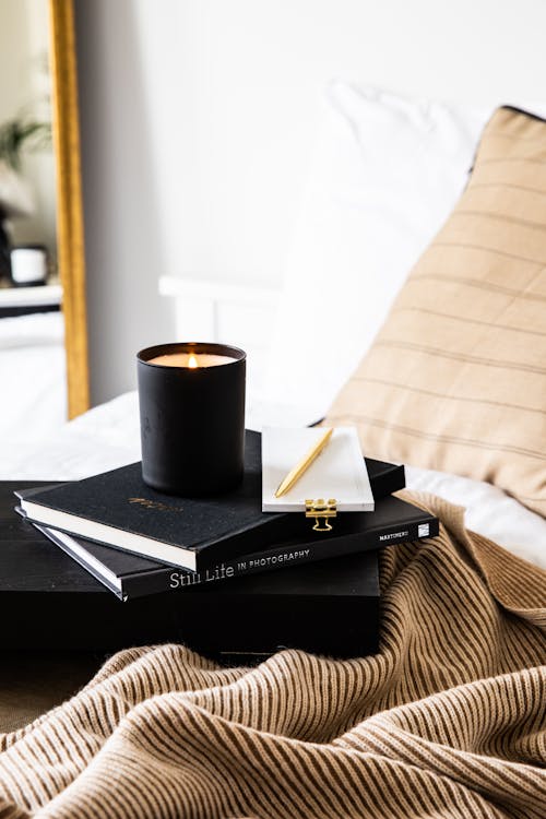 Free Black Books and Burning Candle on Bed Stock Photo