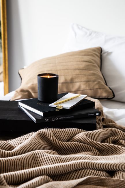 Elegant still life scene with books, candle, and a cozy blanket on a bed, perfect for relaxation.