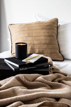 A peaceful bedroom setup featuring a candle, books, and a warm blanket.