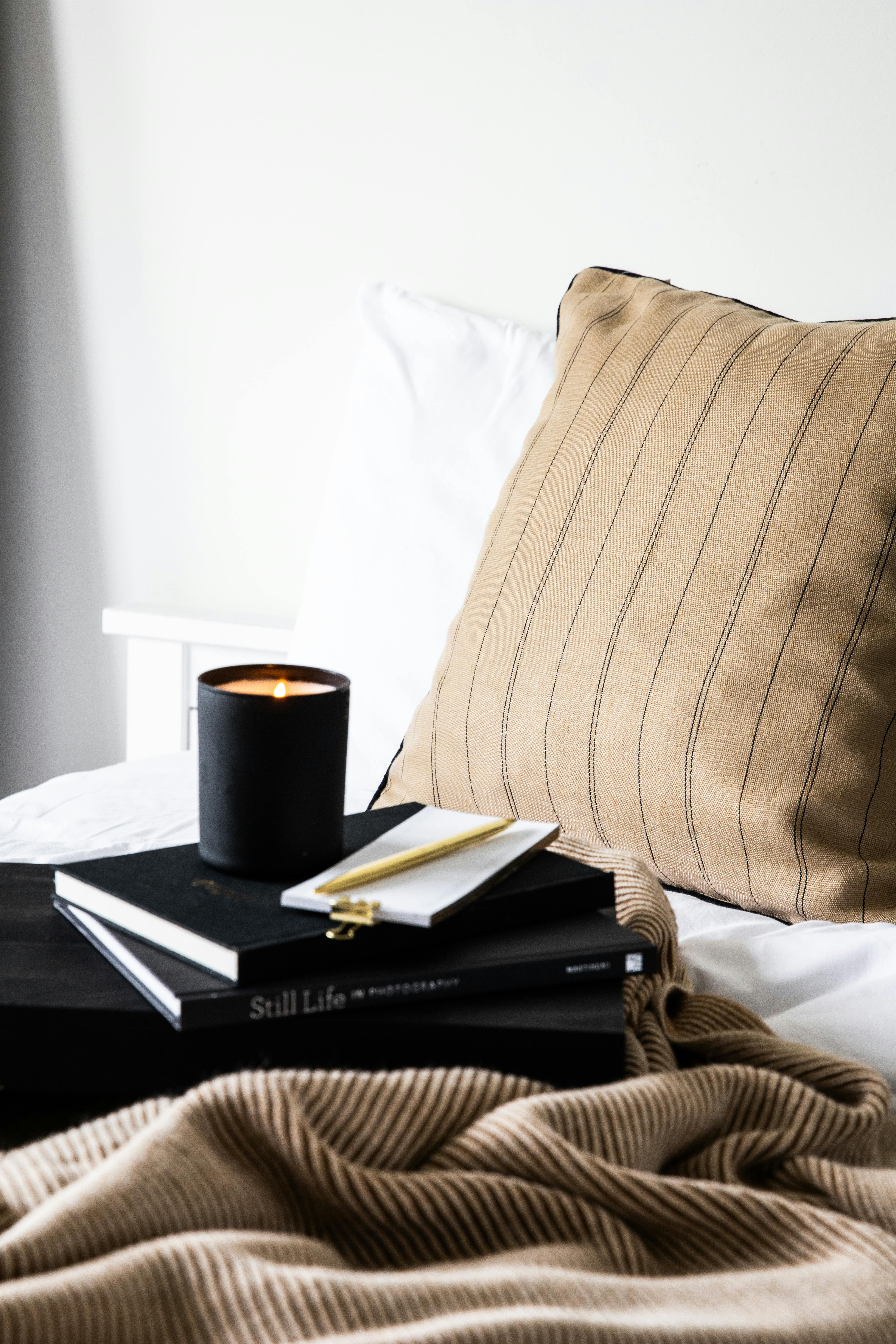A cozy bedroom scene with a candle, books, and blanket on a bed.