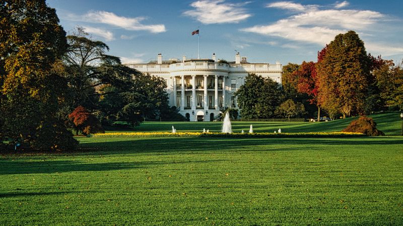 A view of the White House surrounded by autumn foliage and a central fountain in Washington, DC.