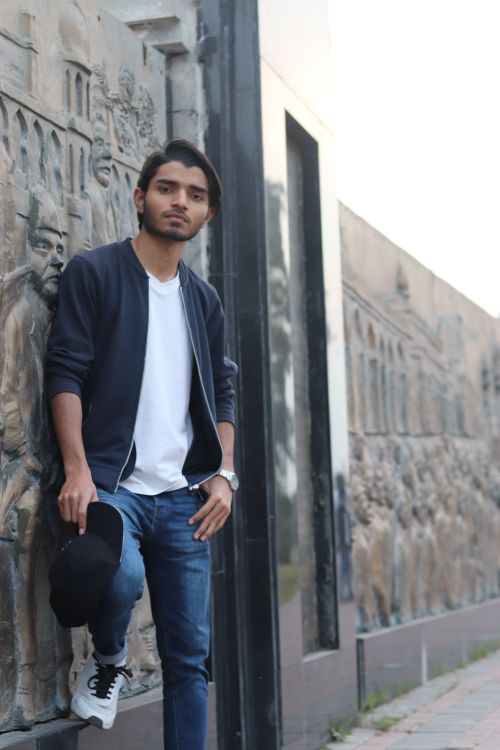 Free Young man in casual attire leaning against a stone wall with intricate carvings. Stock Photo