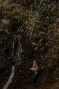 Young Man in Slips Crouching on Steep Slope at Cave