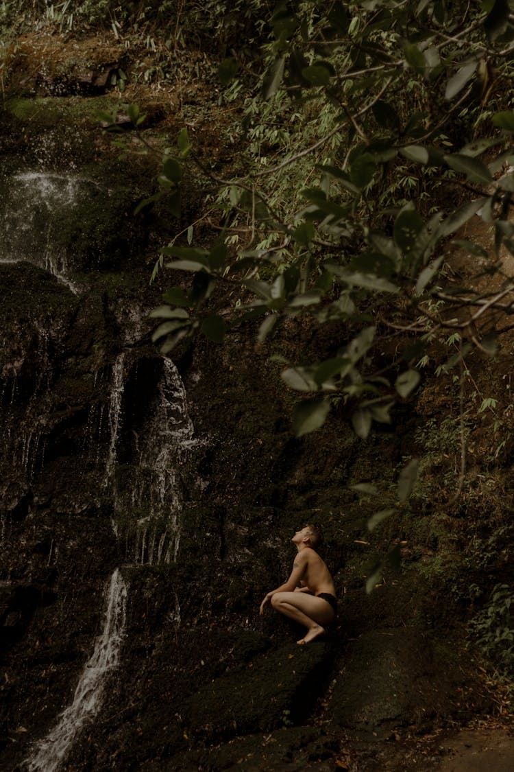 Young Man In Slips Crouching On Steep Slope At Cave