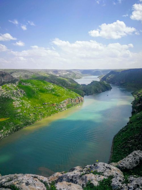 Free A scenic view of a clear river winding through a lush, green valley with distant mountains under a bright blue sky. Stock Photo