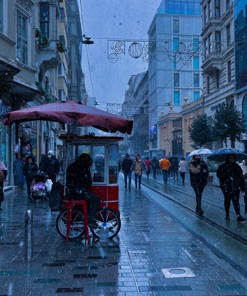 Free A bustling winter street scene with snowfall and a food cart, capturing a vibrant urban atmosphere. Stock Photo