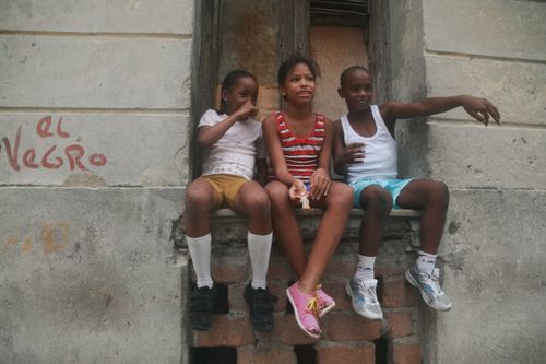 Free Three smiling children sitting on a window sill, enjoying their time together outdoors. Stock Photo