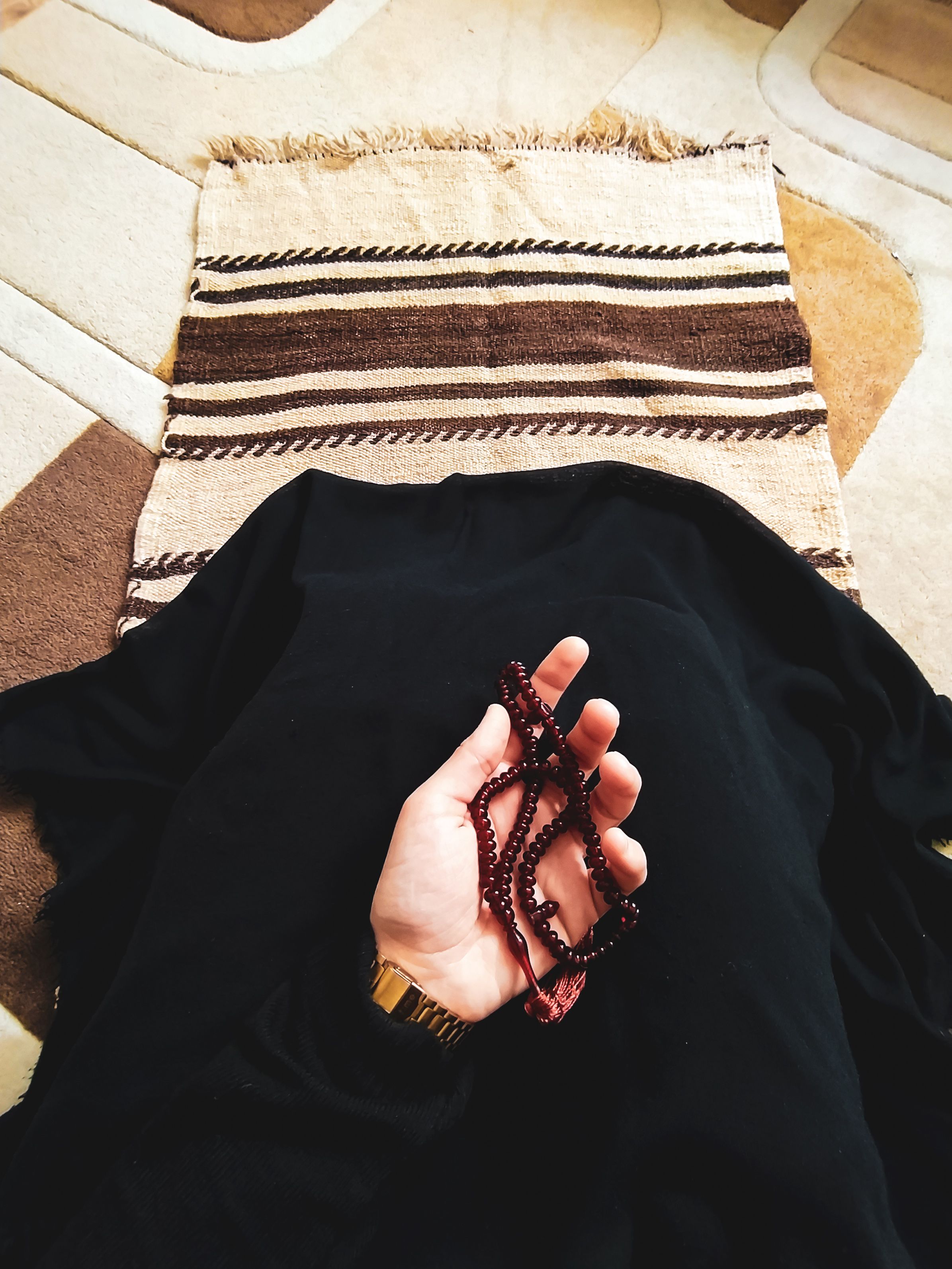 A hand holding tasbih prayer beads on a prayer rug during dhikr and istighfar after salatul tawbah