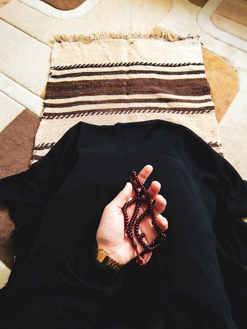 Person Sitting on a Rug and Holding a Rosary 