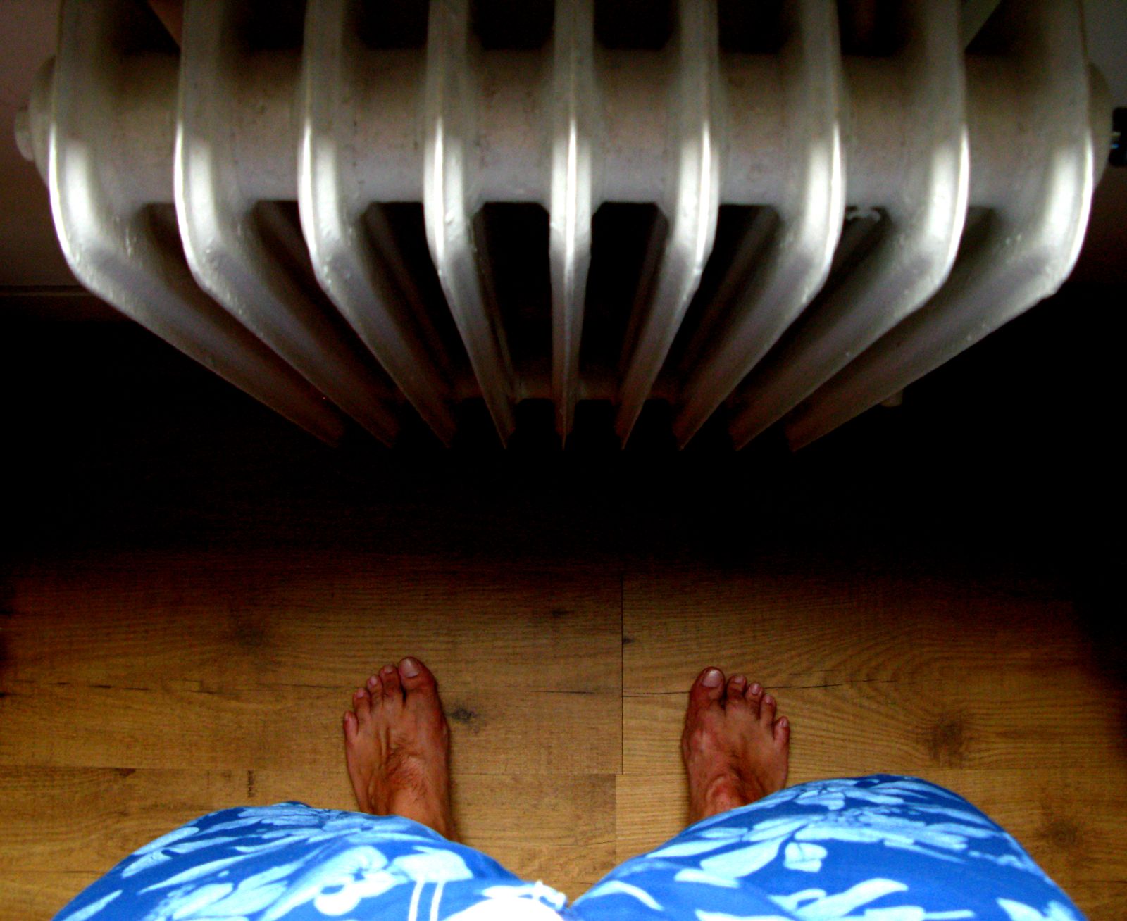 A first-person view of bare feet standing on wooden flooring near a radiator. — How much does an AC repair cost in San Antonio? — US Real Heating & AC, San Antonio