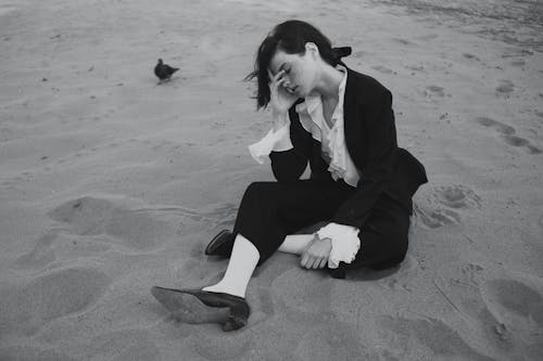 Free Young Brunette Woman in Formal Outfit Sitting on Sand Stock Photo