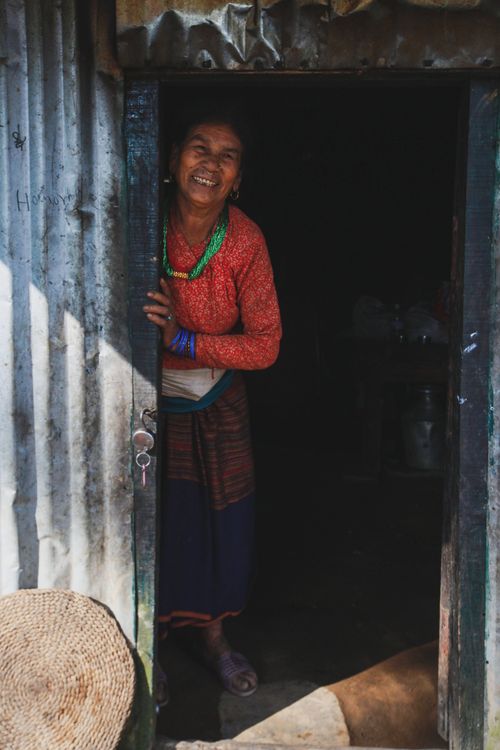 Free A woman in traditional attire smiling warmly as she stands in the doorway of a rustic house. Stock Photo
