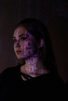 Artistic portrait of a woman with binary code projected on her face in a dark room.