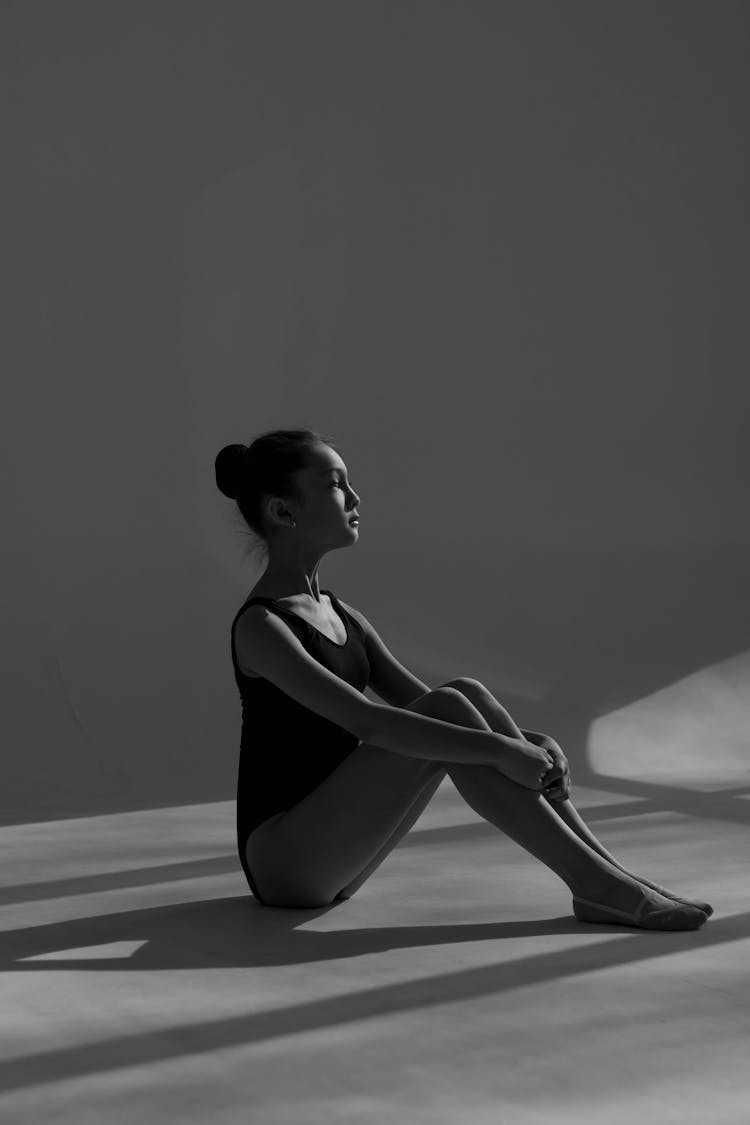 Young Ballerina Sitting On Ground With Straightened Back Hugging Her Knees