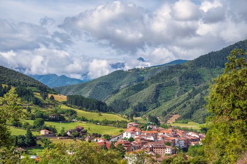 Free Picturesque village nestled in lush green mountains under a cloudy sky, ideal for travel and nature themes. Stock Photo
