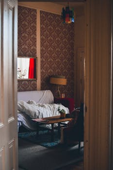 Cozy vintage-themed living room with wallpaper, furniture, and natural light from a window.