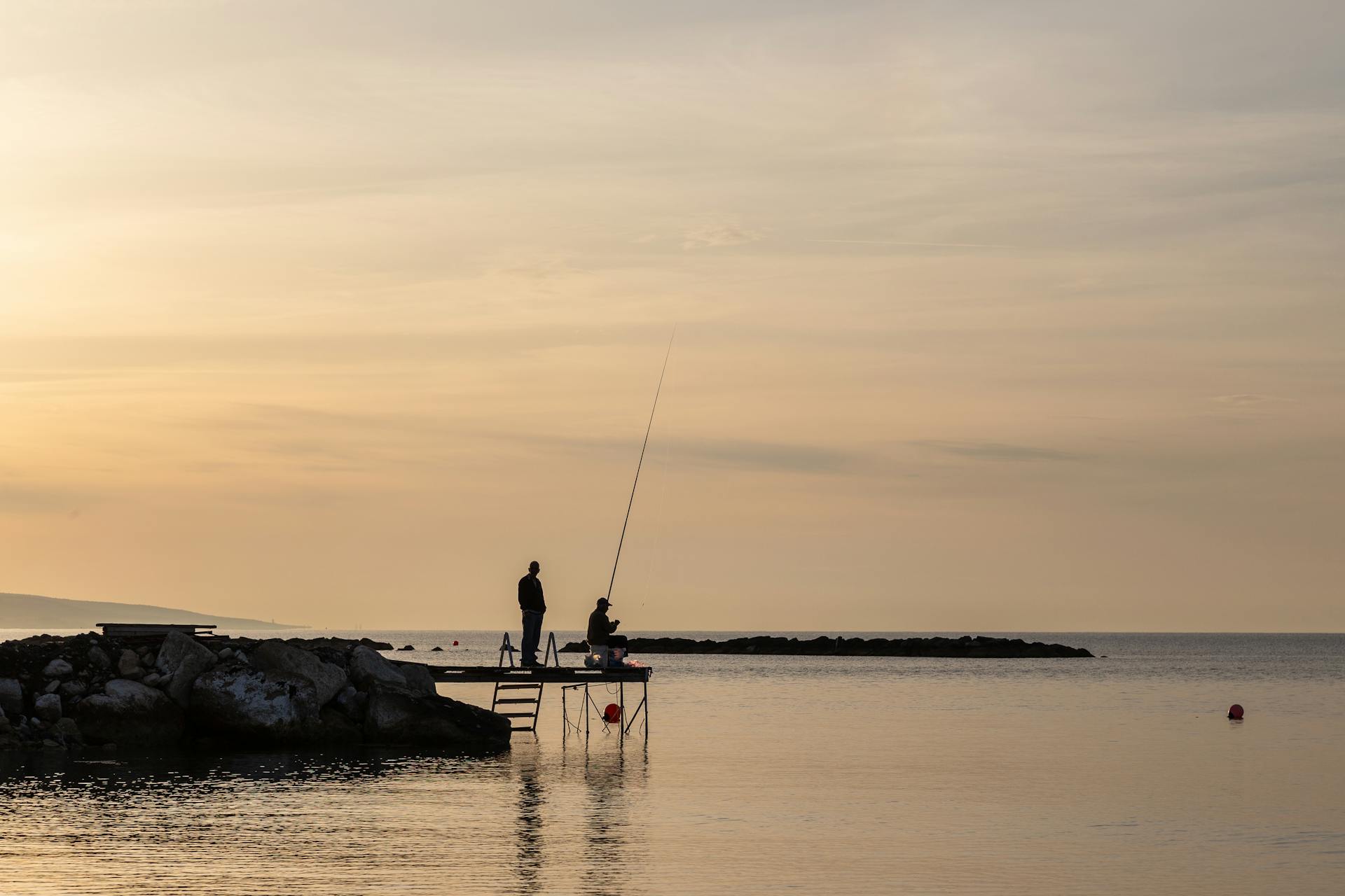 Silhouettes of fishermen fishing at sunset on a Cyprus coastal pier.