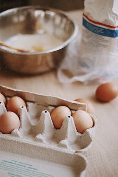 Close-up of fresh eggs in carton with flour and bowl for baking preparation.