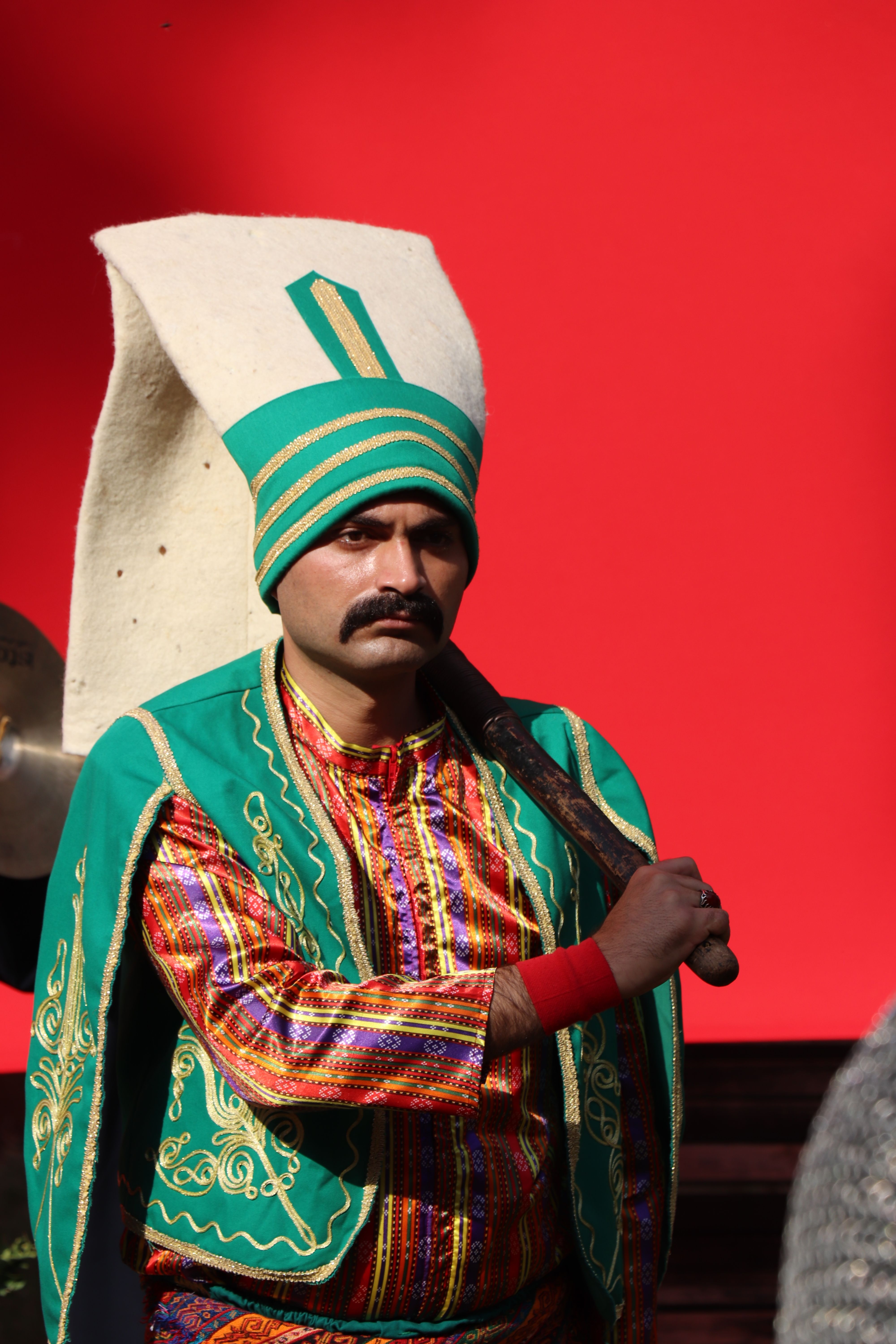 A colorful portrait of a man in traditional Turkish attire against a vibrant red backdrop.