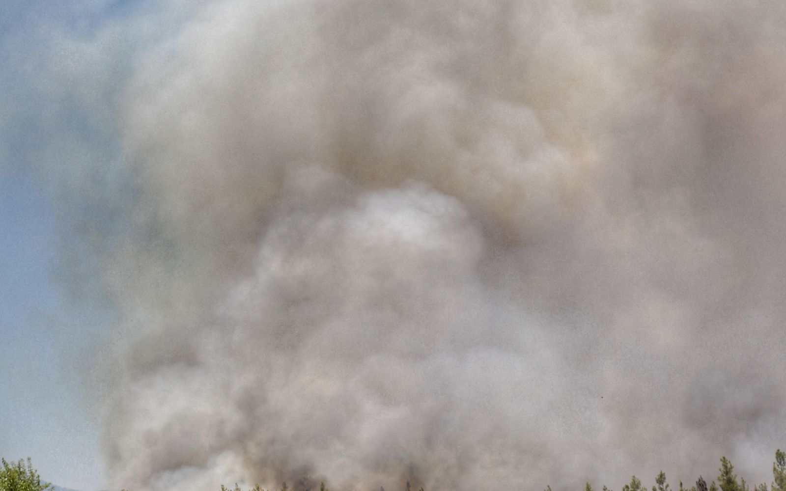White smoke billows from a wildfire spreading across a dry grass field