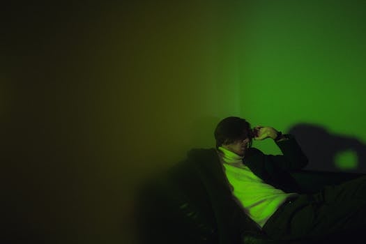 A pensive man sits on a sofa in moody green lighting, creating a dramatic effect.