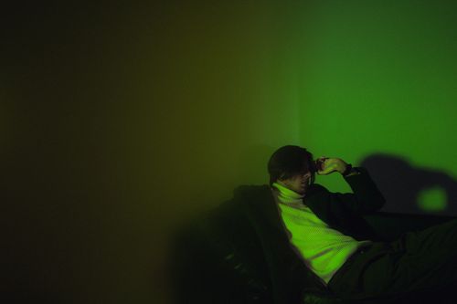 Free A pensive man sits on a sofa in moody green lighting, creating a dramatic effect. Stock Photo