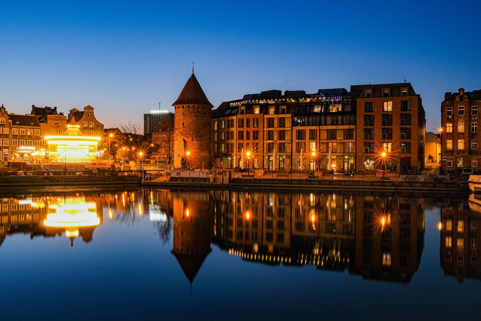 A vibrant twilight view of Gdańsk's riverside architecture reflecting on calm waters in Poland. in Gdansk