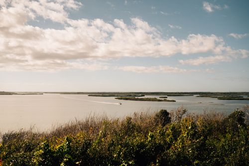 Free A peaceful rural landscape with a motorboat cruising on a calm lake under a cloudy sky. Stock Photo