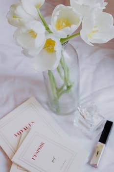 A serene still life featuring white tulips, books, and perfume, perfect for elegant decor themes.