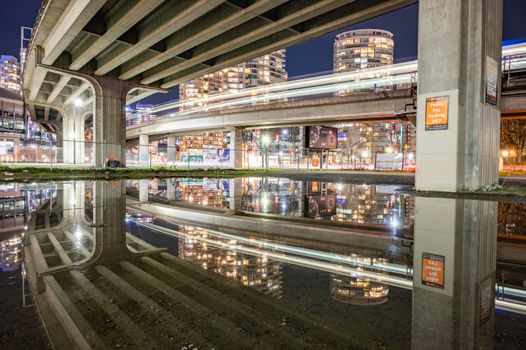 Captivating Vancouver cityscape at night with light trails and reflections under the bridge.