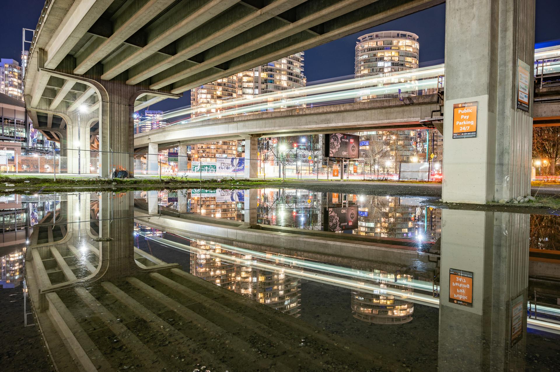 Captivating Vancouver cityscape at night with light trails and reflections under the bridge.