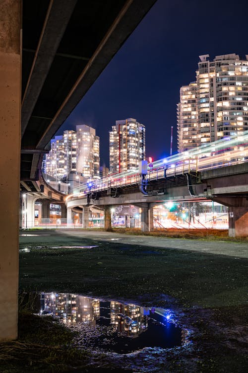 Gray Concrete Bridge Near City Buildings during Night Time