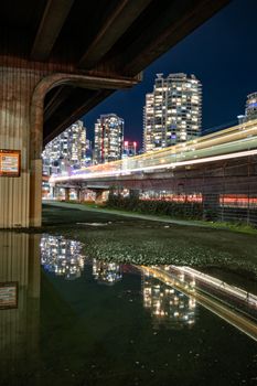 Night view of Vancouver skyline with light trails and skyscraper reflections.