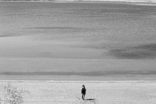 Grayscale Photography of Person Walking Near Body of Water