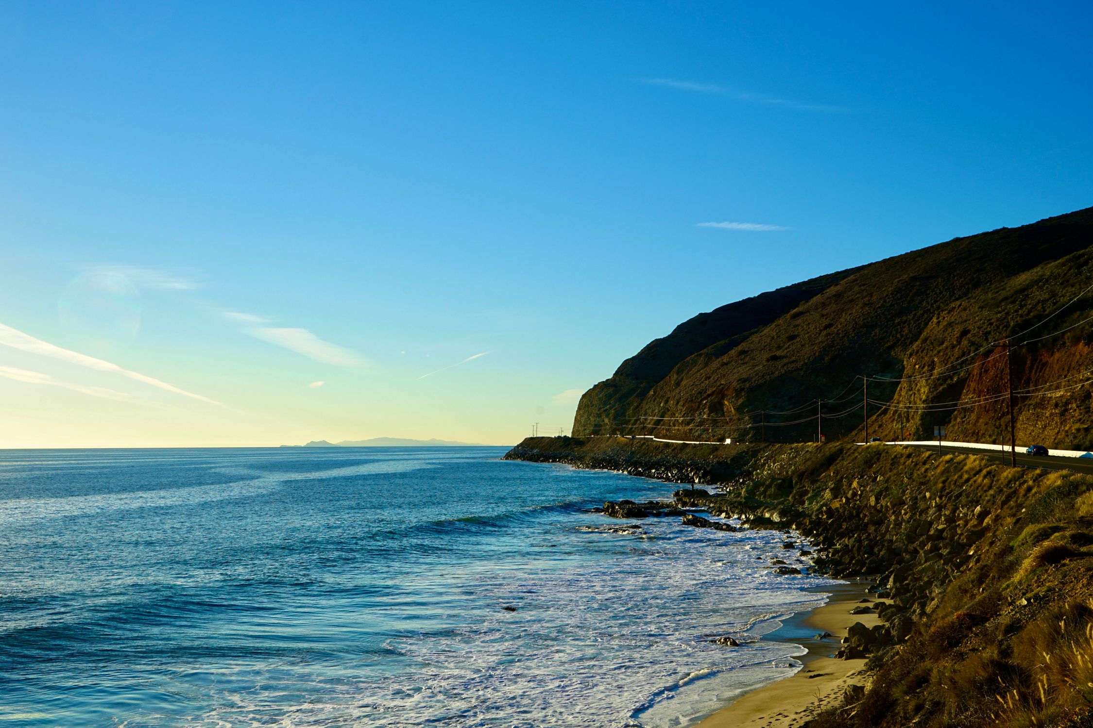 Beautiful coastal view in California with serene ocean waves and a clear blue sky at sunset.