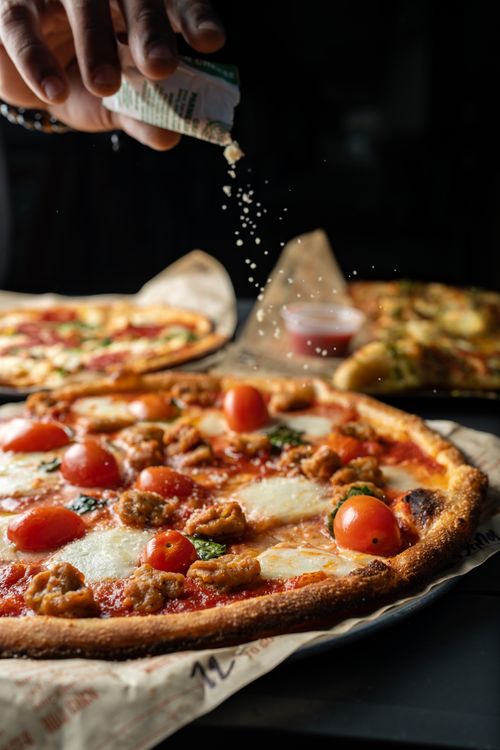 Free Close-up of a freshly baked pizza with cherry tomatoes, mozzarella, and herbs being sprinkled by hand. Stock Photo