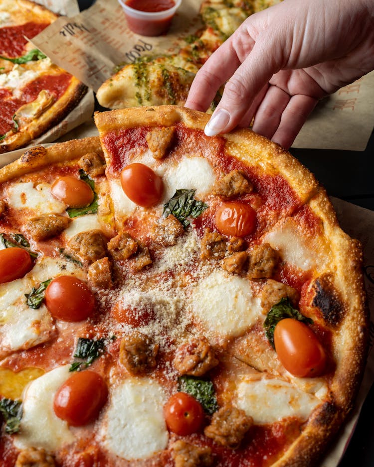 A Person Holding A Sliced Pizza With Tomatoes And Cheese