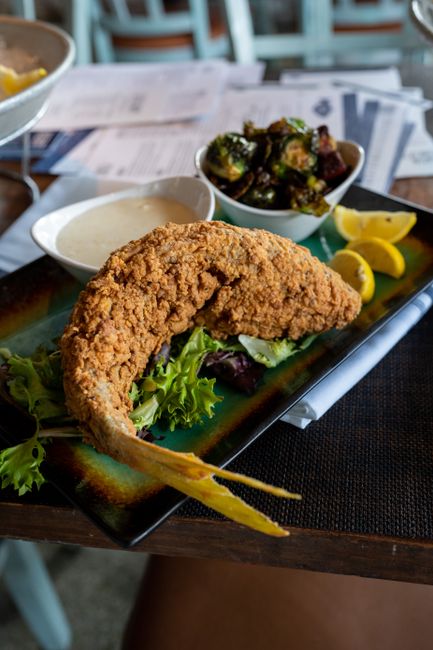 Golden, crisp cornmeal-crusted catfish fillets stacked on a paper-lined plate with lemon wedges and a small bowl of hot sauce alongside.