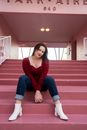 A Woman in a Red Top and Denim Pants Sitting on the Stairs