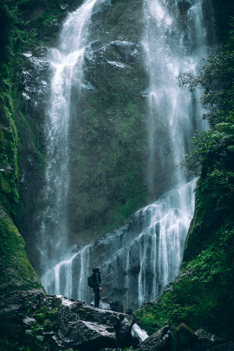 Person Standing On Rock Under Huge Waterfall