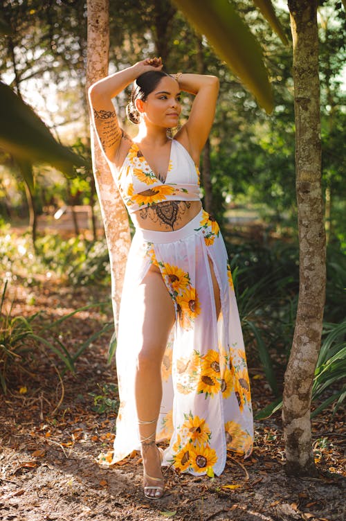 Woman in White and Yellow Floral Dress Standing beside Trees