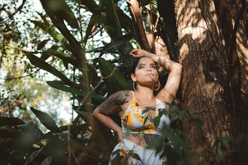 Woman in Yellow and White Dress Leaning on Brown Tree Trunk