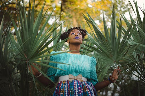 Donna In Una Camicetta Blu E Gonna Multicolore In Posa Con Foglie Di Palmetto